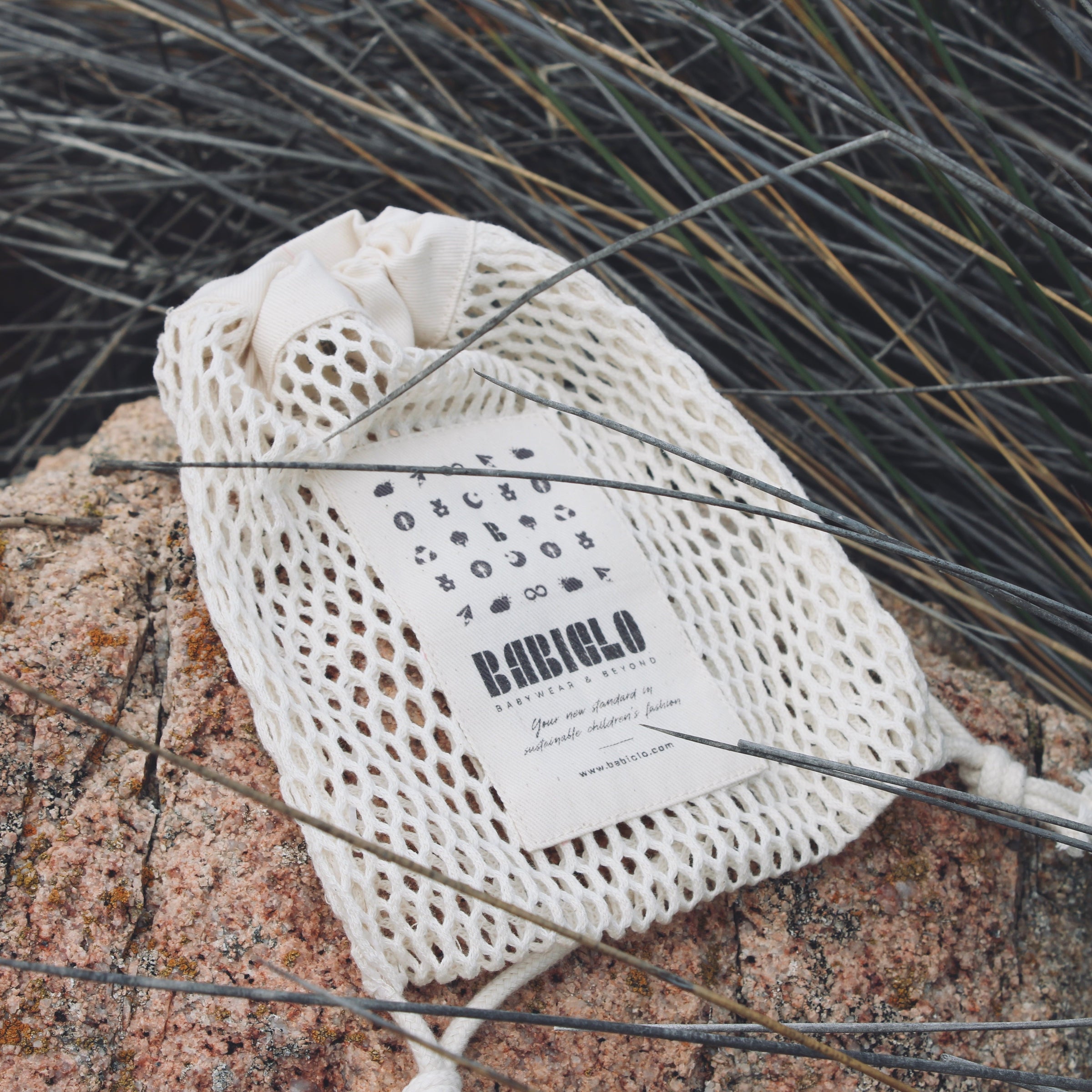 Organic cotton drawstring bag by BABICLO on a rock surface, showcasing sustainable GOTS-certified fabric.