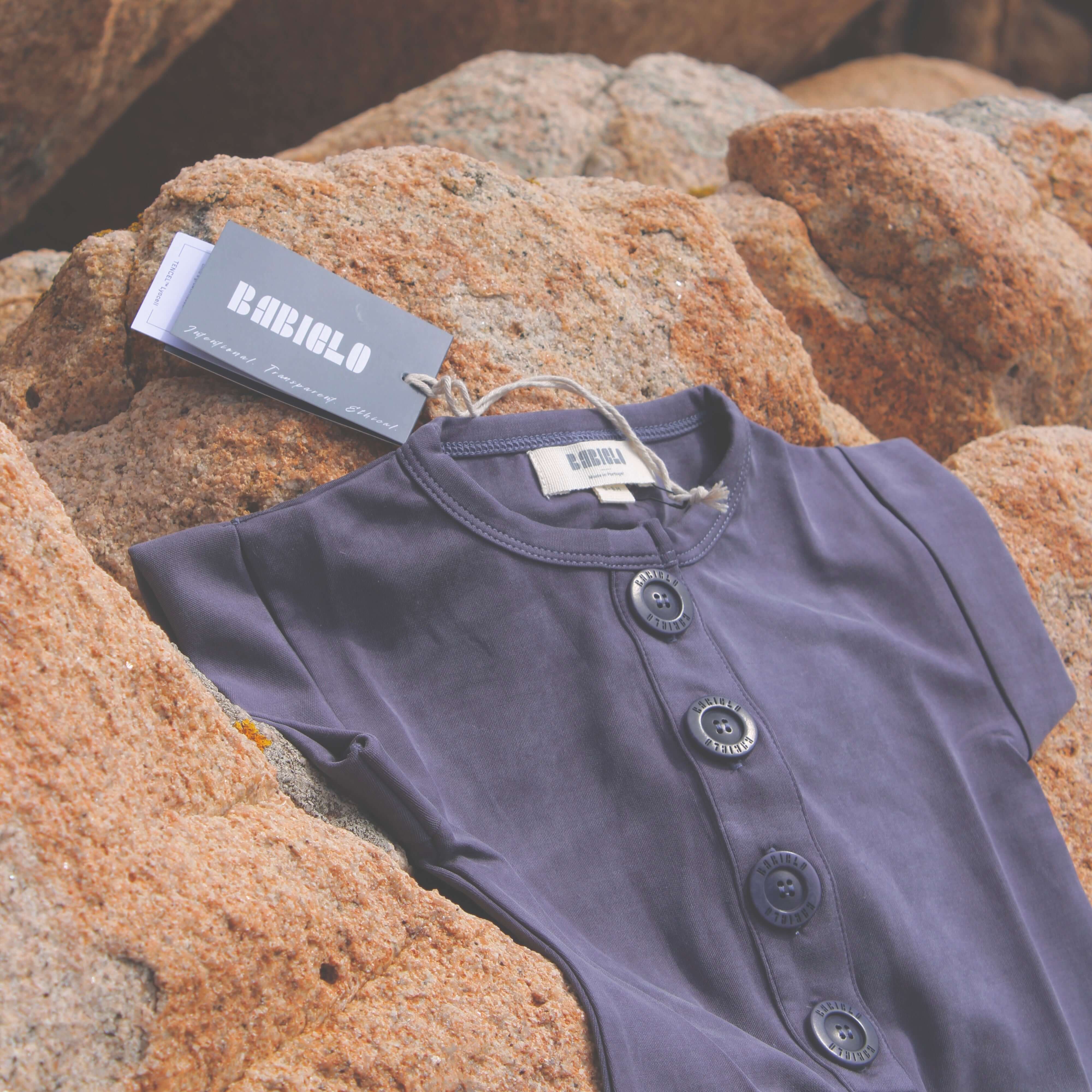 Sustainable children's ready-to-wear: extra-soft romper with buttons on rocky background.