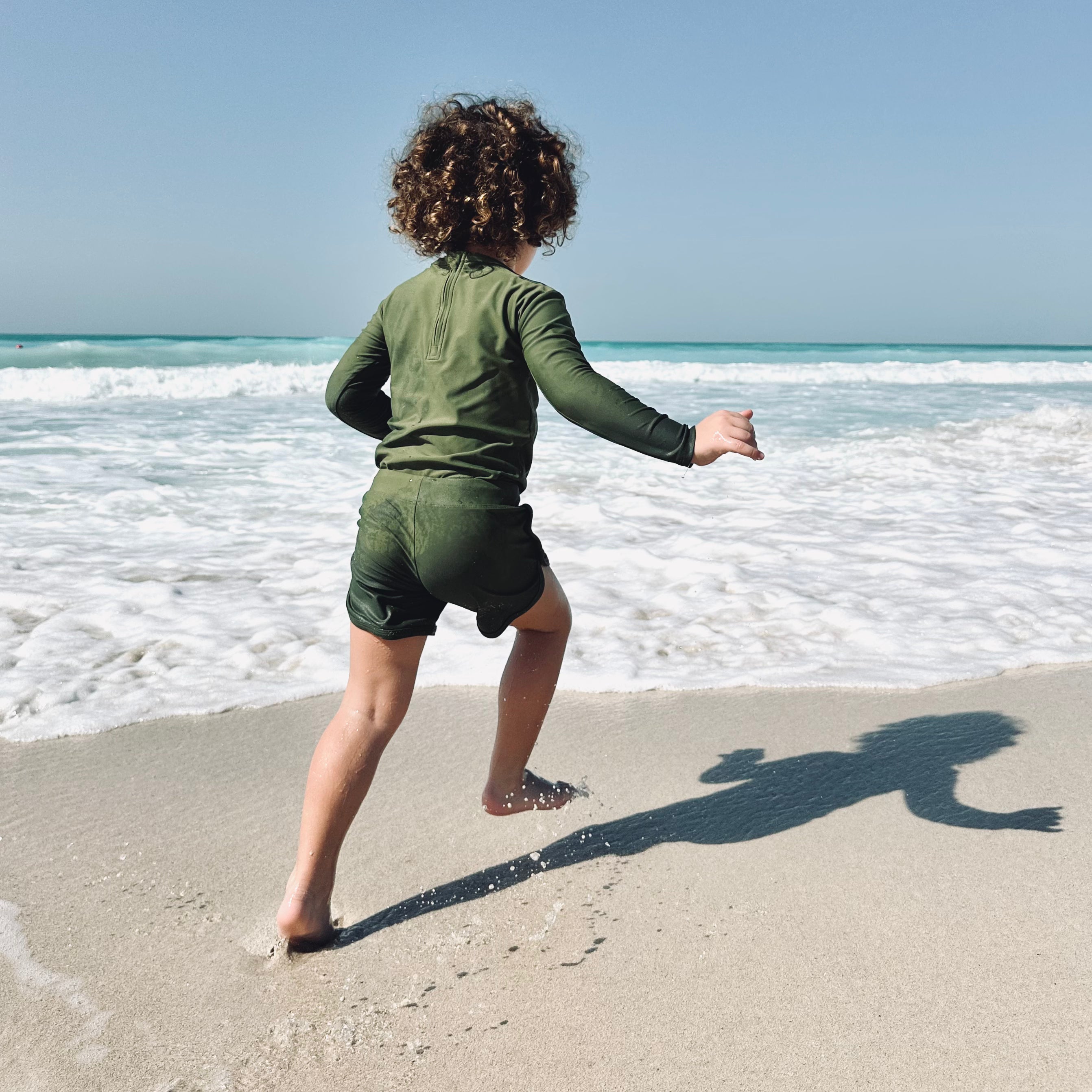 Child playing on the beach in sustainable swimwear from the Sustainable Swimwear Shop for Children collection, featuring ECONYL® fabric.