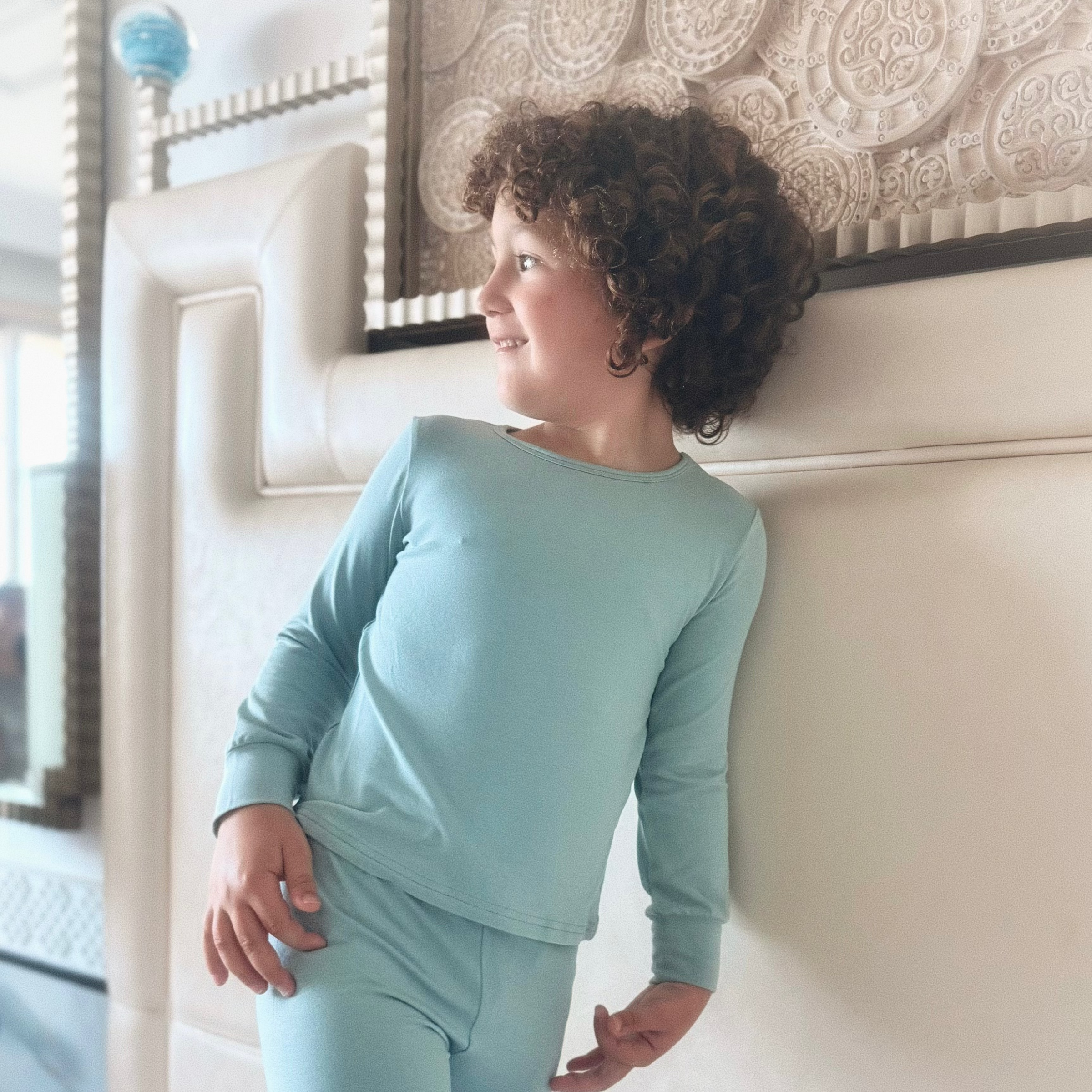 A child wearing TENCEL Micro Modal children pyjamas in a soft blue color, smiling while leaning against a wall.