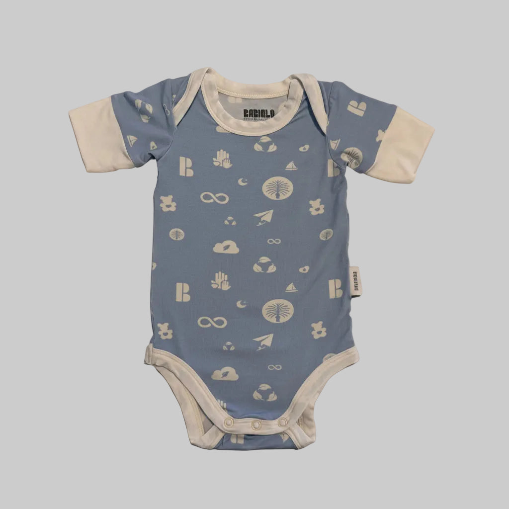 A baby short-sleeve bodysuit laid flat on a light marble surface. The bodysuit has a light blue body with white celestial and abstract prints, and contrasting white sleeves and trim.