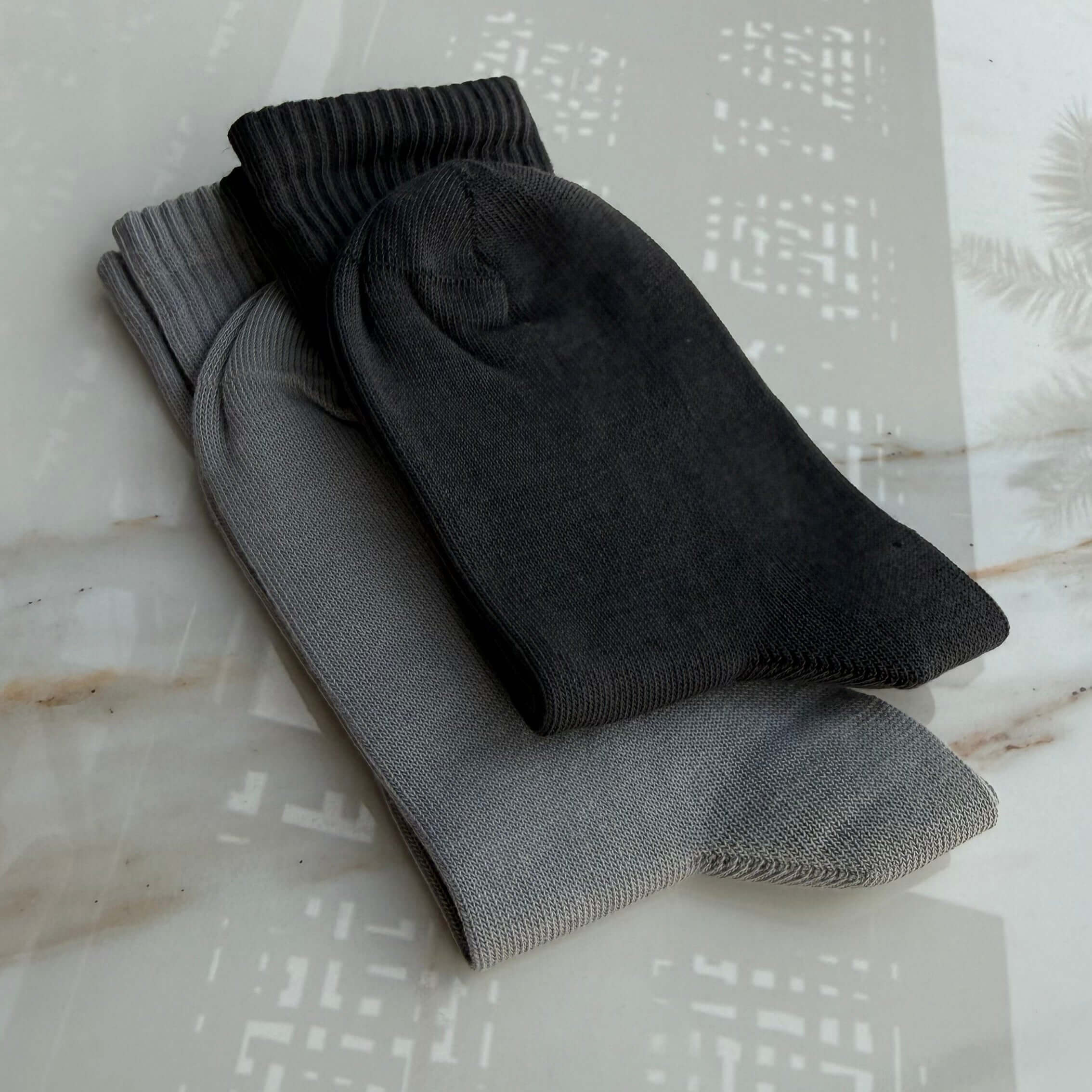 Two pairs of socks, one dark drey and one misty blue, on a textured surface.
