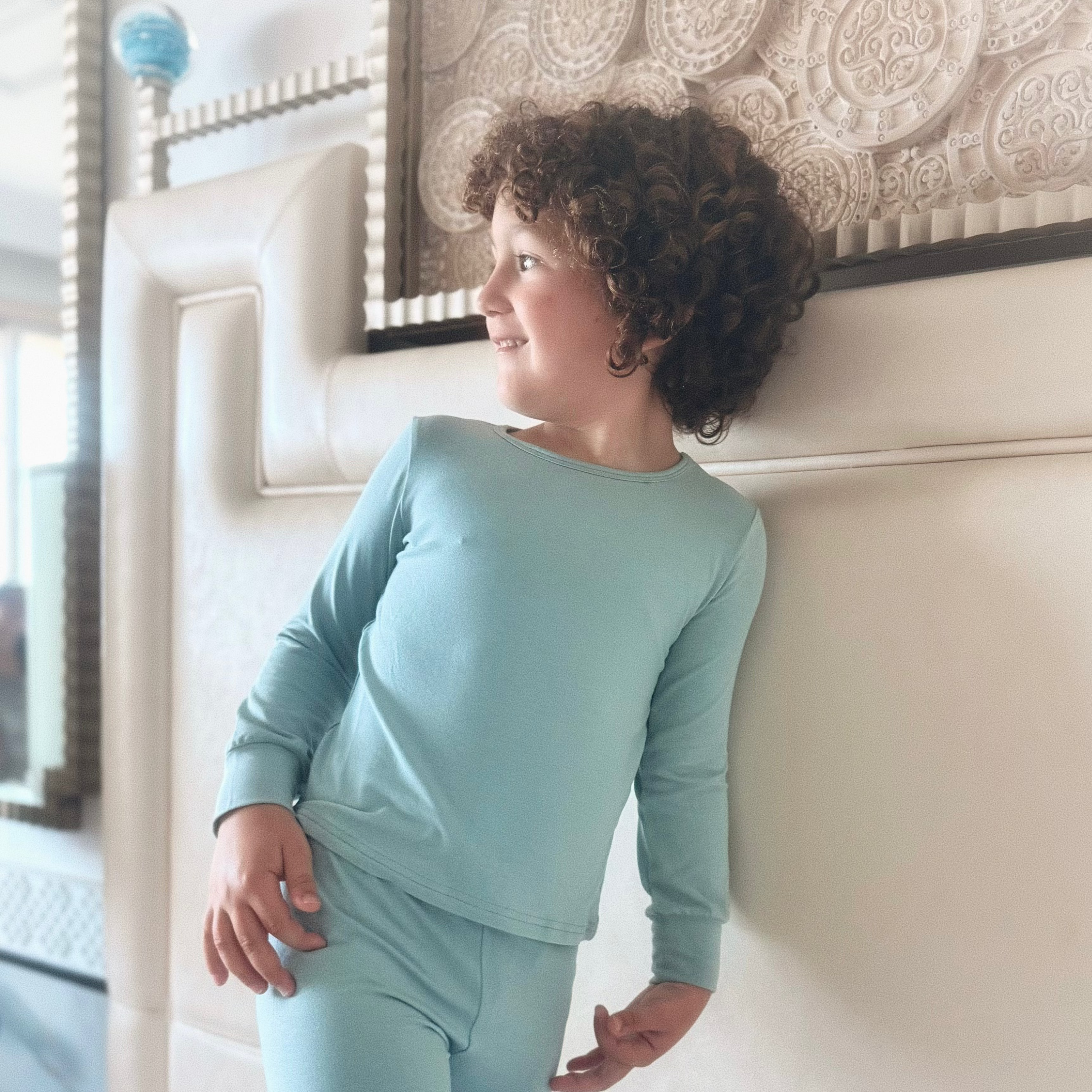 Child wearing a light sage green pyjama in a bedroom setting